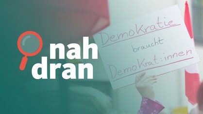 Ein Plakat auf einer Demo vom Wochenende. Darauf steht: "Demokratie braucht Demokrat:innen". Davor das Podcast-Logo von "nah dran".