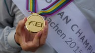 Eine Hand hält eine Goldmedaille der Reit-EM in Aachen.