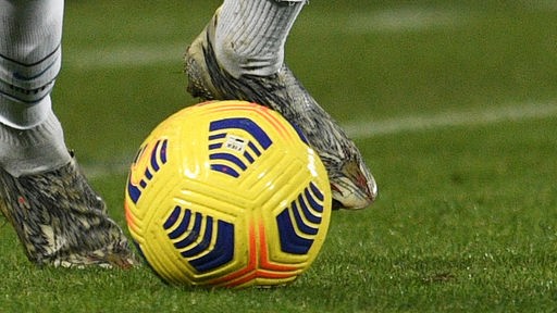 Ein Fußballspieler spielt einen Ball auf einen Spielfeld, zu sehen sind nur die Füße und der Ball