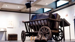 Ein Bollerwagen mit Koffer und Wanderschuhen in der Ausstellung "Von Hier. Von Heimaten und Herkünften" im Clemens Sels Museum Neuss